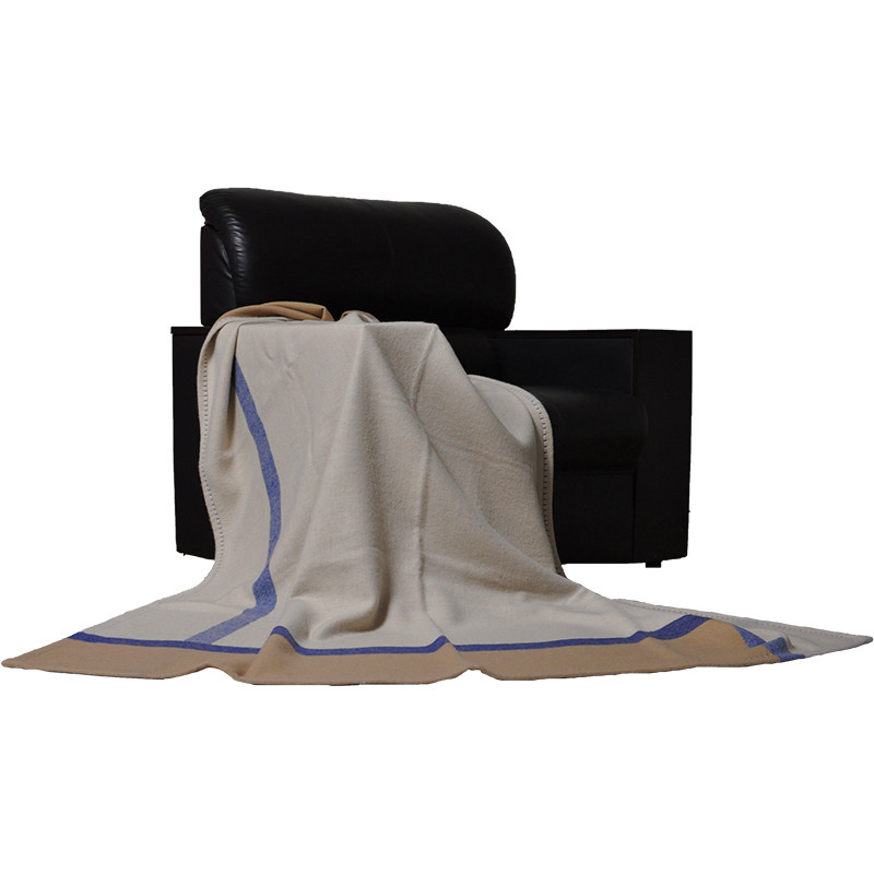 Q0192-A lambswool bed blanket draped over a black chair, displaying its warm-grey surface, blue stripes and camel border.