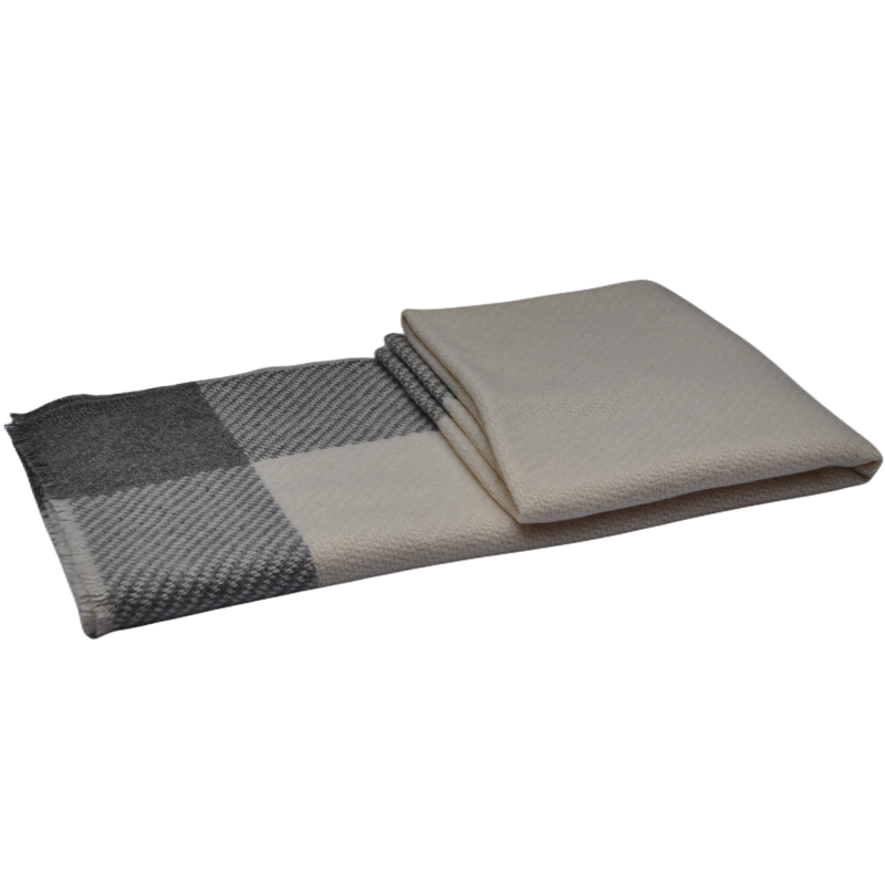 A top-down view of a folded plaid blanket showcasing the intersection of dark grey, light grey, and cream color blocks.