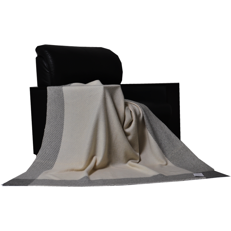 A cream-colored cashmere throw with a grey border draped elegantly over the arm of a black leather chair.