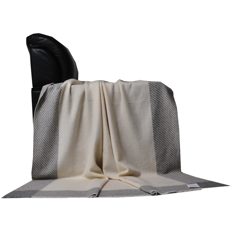 A front view of the cashmere throw draped over a black sofa, highlighting the wide grey vertical stripes on a cream base.