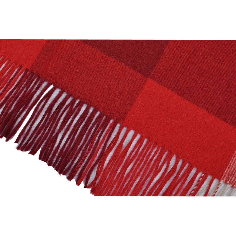 Detailed view of handcrafted tassels and fringe on a red checkered wool blanket.