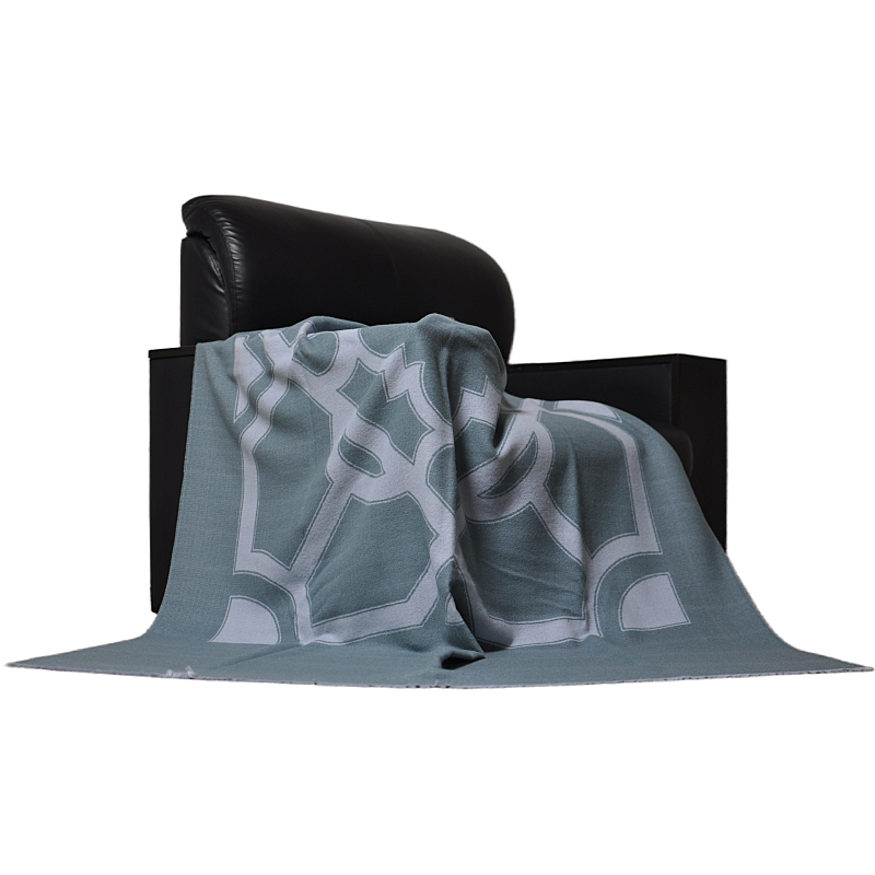 Side view of the TDX2203 grey-green geometric patterned throw blanket draped over a black chair.