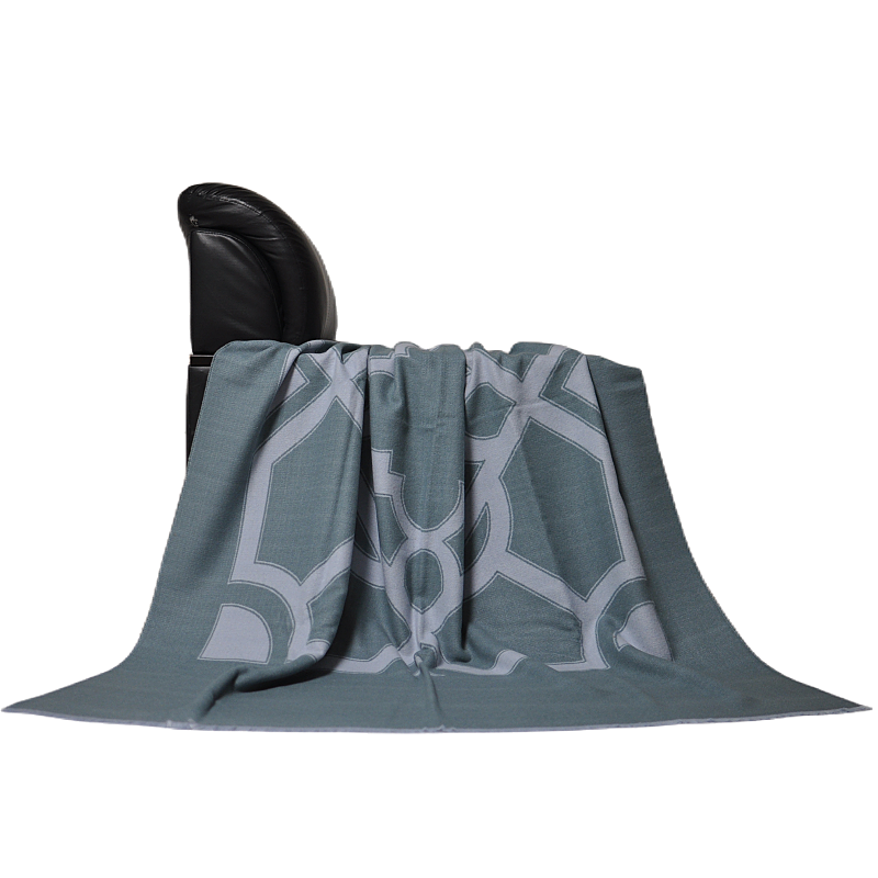 DX2203 grey-green geometric patterned throw blanket draped naturally over the back of a black chair.