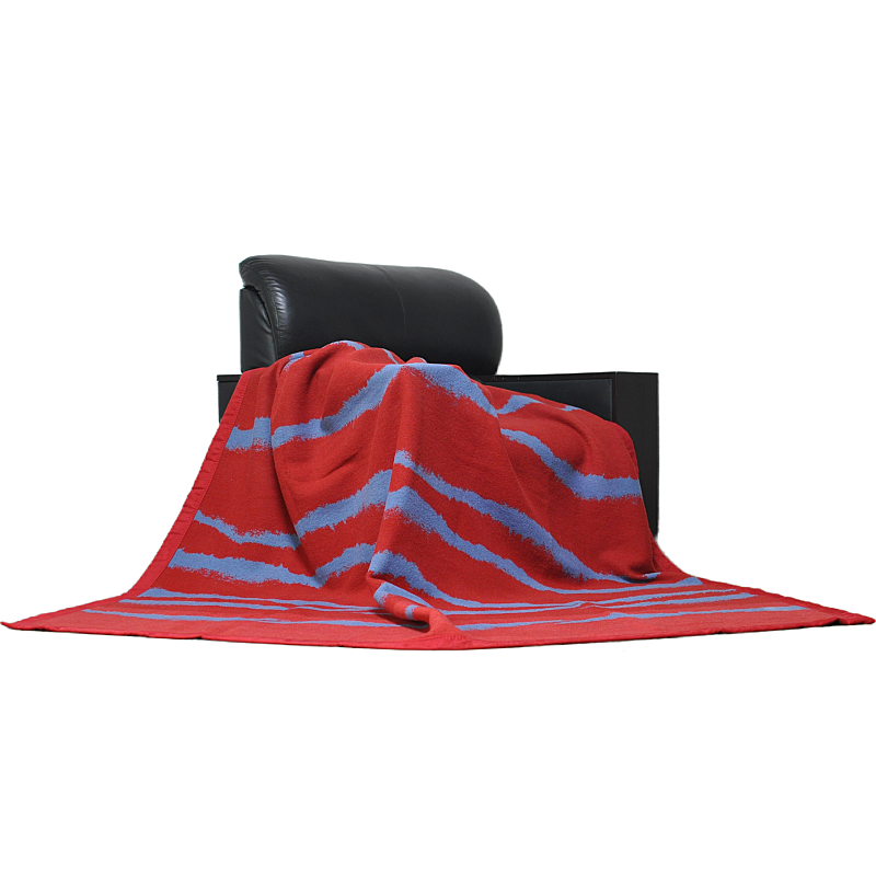 Red and grey wave-pattern wool throw blanket draped over a black armchair.
